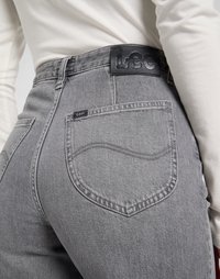 Los jeans de mezclilla gris cuentan con una cintura alta, bolsillos traseros curvados y una etiqueta de cuero negro en la cintura. La tela tiene una textura suave.