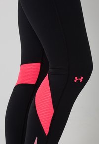Leggings sportivi neri con pannelli testurizzati rosa brillante sulle cosce e sui polpacci, caratterizzati da un piccolo logo Under Armour rosa sulla gamba destra.