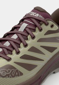 Scarpa da corsa Hoka One in verde e marrone con tomaia texturizzata, lati decorati, lacci bordeaux e suola leggera e ammortizzata.