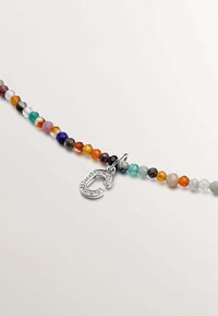 Pulsera de cuentas con piedras facetadas de colores variados y un charm en forma de "C" acentuado con gemas en plata. Textura suave y formas variadas.