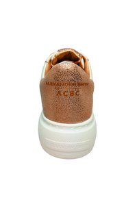 Weiße Sneakers mit einer strukturierten rose-goldenen Kunstleder-Ferse, die "ALEXANDER SMITH" geprägt hat, und einer weißen Gummisohle mit strukturiertem Grip.