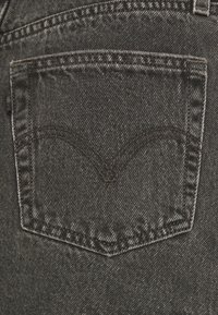 Svart denimjean ficka med en blekt textur. Har mörka sömmar i ett igenkännbart bågmönster och synliga nitar längs kanten.