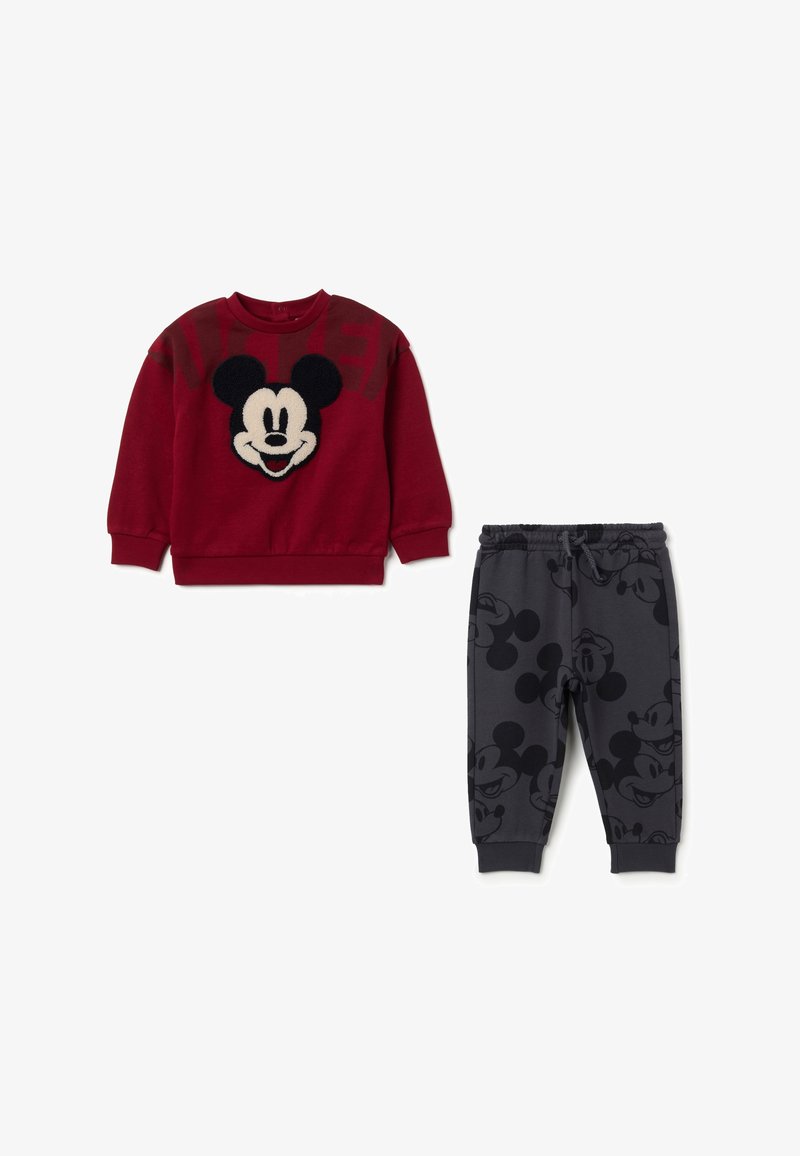 Rode sweatshirt met een fuzzy Mickey Mouse gezicht, gecombineerd met grijze broeken met een herhalend Mickey Mouse patroon. Zachte katoenmix stof.