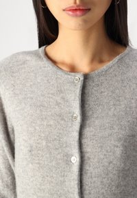 Jasnoszara wełniana kardigan z okrągłym dekoltem, pięcioma guzikami z przodu oraz miękkim, teksturowanym materiałem. Zbliżenie na górną część.