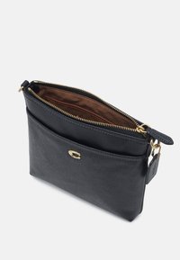 Černá kožená taštička se zipovým uzávěrem, zlatými detaily, přední kapsou a hladkým povrchem; vnitřek má hnědou podšívku.