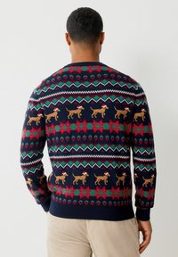 Marineblauer Pullover mit einem festlichen Muster aus roten und grünen geometrischen Designs und braunen Hunden, die Weihnachtsmützen tragen, über den Rücken.
