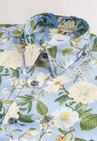 Skjorte med blomstermønster på blå baggrund, med hvide blomster, blade og en bi. Bomuldsmateriale, knappet krave med grå knapper.