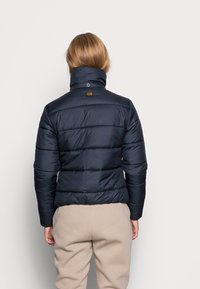 Jacka med puffig design i mörk marinblått, med hög krage och quiltat mönster. Noterbart logotags på baksidan, med en mjuk och glänsande yta.