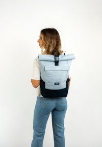 Rucsac cu capac rabatabil, de culoare albastră deschisă, cu accente de albastru închis. Fabricat din material durabil, având un buzunar frontal și bretele ajustabile.