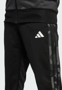 Černé sportovní kalhoty s texturovanou tkaninou, třemi bílými pruhy a maskáčovým vzorem po stranách; s bílým logem.