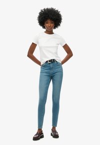 Pantalones vaqueros ajustados de denim azul con una cintura alta, combinados con una camiseta de algodón blanca entallada y mocasines marrones con suela gruesa.