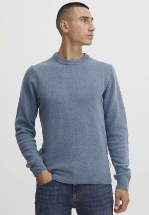 Pulover albastru deschis, fabricat dintr-un material moale, cu guler rotund și manșete și tiv zimțat. Purtați-l cu blugi albastru închis.