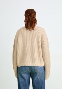 Maglione a coste beige con spalle cadenti. Abbinato a jeans in denim blu, che mostrano una vestibilità comoda e una consistenza morbida.