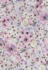 Blumenhemd mit Knopfleiste, das ein pastelliges Muster aus rosa, lila und schwarzen Blumen auf einem hellen Hintergrund zeigt. An der Vorderseite befinden sich Plastikknöpfe.