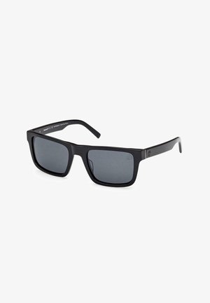 Gafas de sol negras con montura cuadrada, lentes oscuros y brazos de plástico elegantes con un sutil detalle de marca.