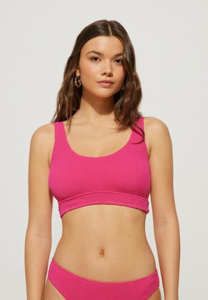 Rosa gestrickter Bikini-Oberteil mit Rundhalsausschnitt und breiten Trägern, der ein strukturiertes Muster aufweist. Der Stoff wirkt dehnbar und körperbetont.