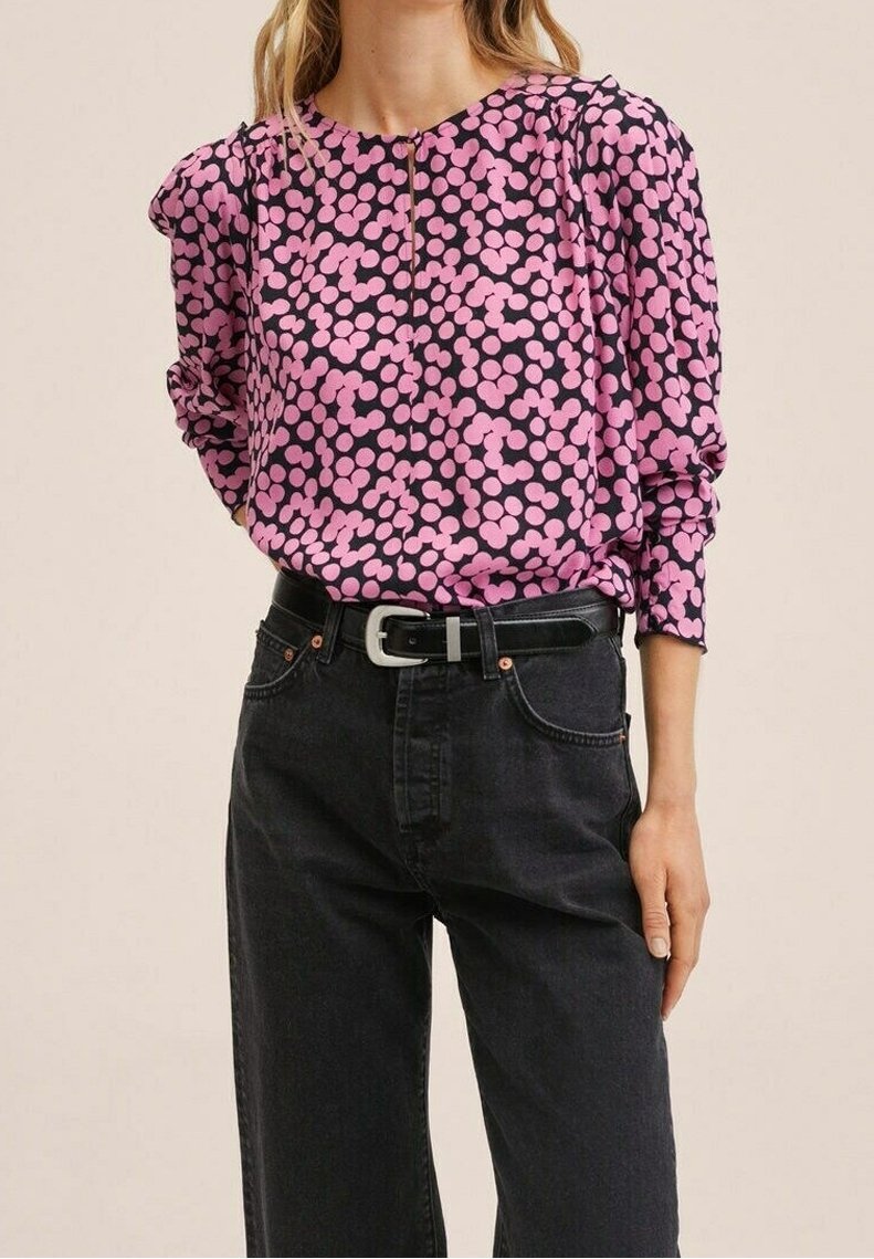 Blouse rose à pois noirs en tissu léger ; manches bouffantes et col zippé, associée à un jean noir taille haute.