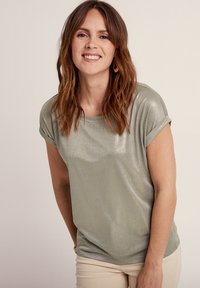 T-shirt a maniche corte di un verde chiaro con una leggera lucentezza. Tessuto morbido, scollatura rotonda e risvolti. Abbinato a pantaloni color crema.