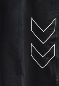 Nærbillede af sort stof med to hvide omridsede nedadvendte chevronformer på højre side.