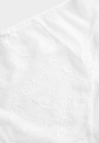 Vitt spetstyg med blommönster, mjuk textur och en satängrosett. Designen är delikat och lager-på-lager med en genomskinlig kvalitet.