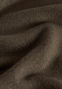 Primer plano de tela de punto marrón oscuro con textura visible y pliegues que crean sombras suaves.