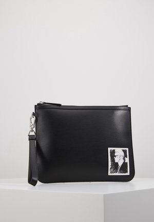 Schwarze rechteckige Lederclutch mit Handgelenkschlaufe und kleinem weißen Patch mit einer schwarz-weißen Skizze einer Person im Profil.