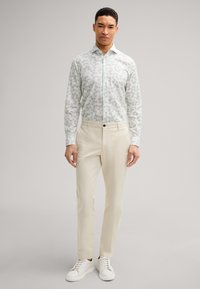 Blumenmuster-Hemd in Hellgrün und Weiß, kombiniert mit beigen Hosen und weißen Sneakers. Glatte Stoffqualität und taillierte Passform.