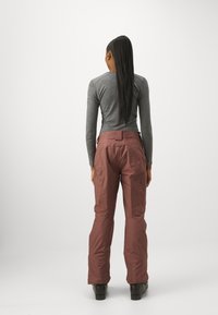 Brune ski bukser med høj talje, sidelommer og et strømlinet design. Stoffet ser glat og vejrbestandigt ud, parret med sorte sko.