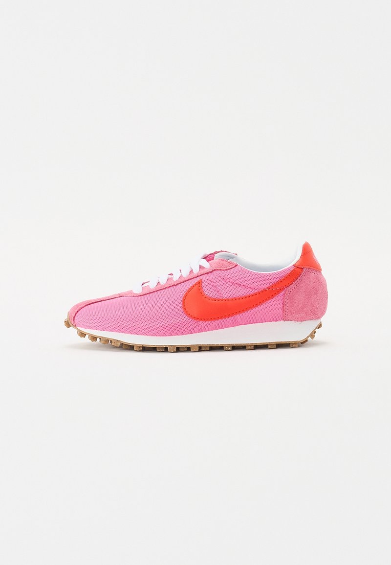 Chaussure de running Nike basse rose et rouge avec lacets blancs et semelle texturée marron, vue de côté sur fond blanc.