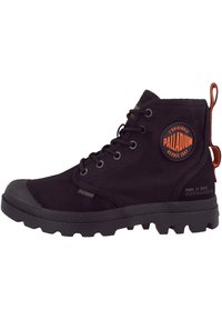 Bottines en tissu noir avec un embout en caoutchouc, tige texturée, œillets en métal ronds et écusson orange sur le côté ; semelle épaisse et à motifs.