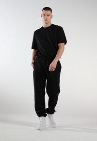 Schwarzes Baumwoll-T-Shirt im relaxed Fit, kombiniert mit schwarzen Sweatpants mit einem elastischen Bund, Modell trägt weiße Sneakers.