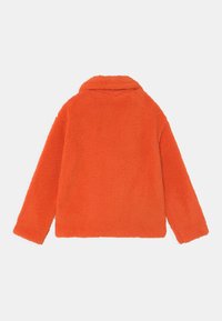 Pomarańczowa polarowa kurtka z kołnierzykiem i długimi rękawami, wykonana z miękkiego, teksturowanego materiału i o pudełkowym kroju.
