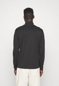 Polo a maniche lunghe nera realizzata in tessuto morbido, con collo alto e maniche aderenti, caratterizzata da un design pulito e minimalista.