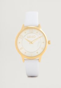 Ceas aurit cu cadran rotund alb, curea din piele albă și marcaje cu numere arabe. Prezintă cristale mici la pozițiile 3, 6, 9 și 12.