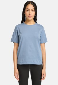 Lyseblå bomulds-t-shirt med korte ærmer, der har en rund halsudskæring og et lille broderet logo på venstre bryst. Glat tekstur.