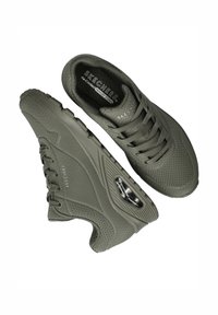 Grijze Skechers sportschoenen met een perforeerde bovenkant, gevoerde zolen en een zichtbare luchtkoelingseenheid aan de zijkant, gepositioneerd voor boven- en zijaanzichten.