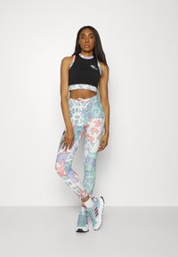 Top atlético preto cropped com leggings coloridas apresentando padrões abstratos em tons pastéis. Ténis azul claro completam o conjunto.