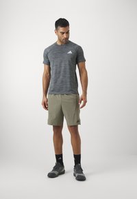 Grå stribet kortærmet atletisk T-shirt med hvidt logo, parret med khaki shorts. Komposit sko og sorte sokker fuldender outfittet.