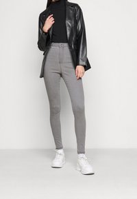 Jeans grises de cintura alta con un corte slim, combinados con un suéter negro de cuello alto y una blazer negra de cuero sintético. Zapatillas blancas completan el look.