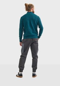 Pullover en polaire teal avec un col haut associé à un pantalon cargo gris comportant des poches latérales et des poignets élastiques. Baskets noir et blanc.