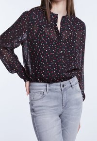 Musta läpikuultava paita nappimetalla, jossa on värikkäitä sydänkuvioita. Yhdistetty vaaleanharmaisiin slim fit -farkkuihin.