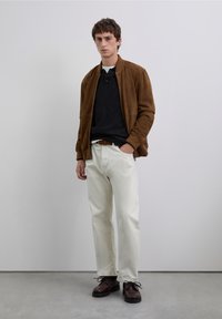 Brown suede bomber jacket over a dark sweater, paired with light-colored pants and brown lace-up shoes. Smooth texture throughout.