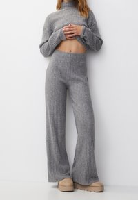 Grijs geribbeld tricot tweedelige set met een cropped turtleneck trui en hoge taille wijde broek. Gladde textuur en relaxte pasvorm.