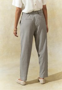 Pantalons à carreaux noir et blanc avec une coupe décontractée, dotés d'une taille à cordon de serrage et de poches arrière, associés à des chaussures slip-on beiges.