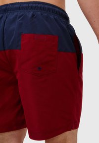 Svømmbukser med et burgunder og marineblå fargeblokkdesign. Laget av lett stoff med elastisk midjebånd og baklomme.