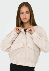 Lichtbeige cropped jack met een gestructureerd ontwerp, voorzien van twee voorzakken, drukknoopsluitingen en een elastische tailleband. Glad stoftextuur.