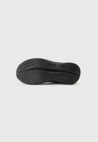 Semelle de chaussure en caoutchouc noir avec un motif texturé, comprenant des rainures et des points de grip circulaires pour une adhérence optimale. Forme évasée au niveau du talon.