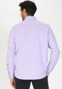 Chemise à manches longues lilas avec un col boutonné, dotée d'une texture lisse et d'un petit logo sur le poignet gauche.