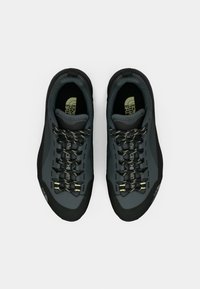 Szürke technikai túracipők sima felsőrésszel, megerősített fekete gumitalppal az orr részen, és fényvisszaverő fűzőkkel, melyeken sárga díszítések találhatók.