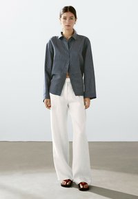 Navy striped button-up shirt with an oversized cut, paired with white vertical-striped wide-leg pants and brown slide sandals.